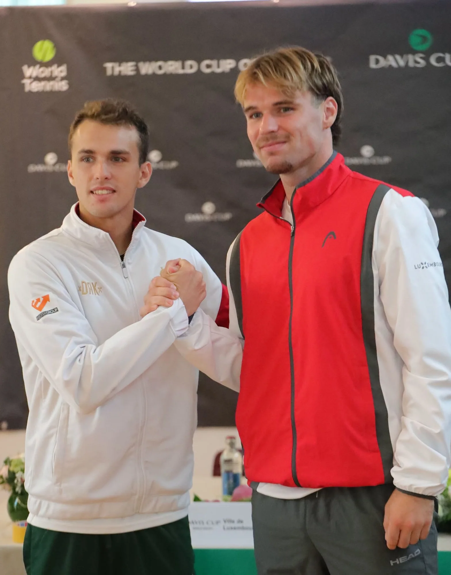 Deux joueurs de Coupe Davis se serrent la main devant le panneau World Cup of Tennis a Luxembourg