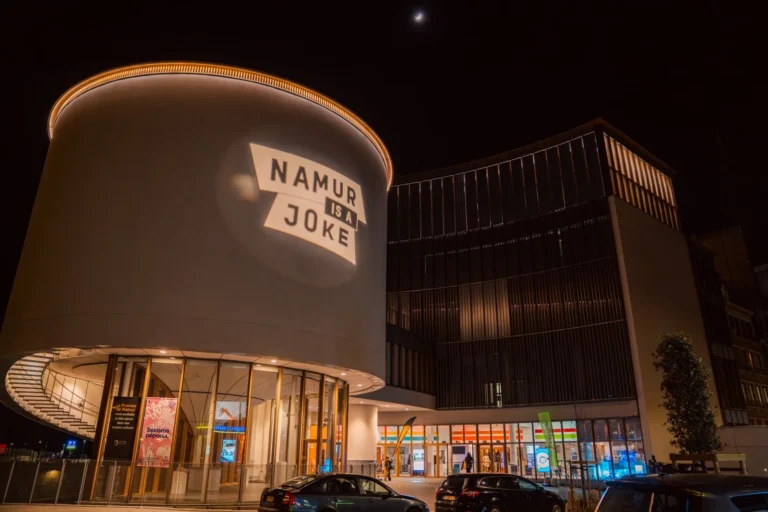 Le bâtiment du Delta à Namur, de nuit, avec le logo Namur is a Joke projeté sur sa rotonde