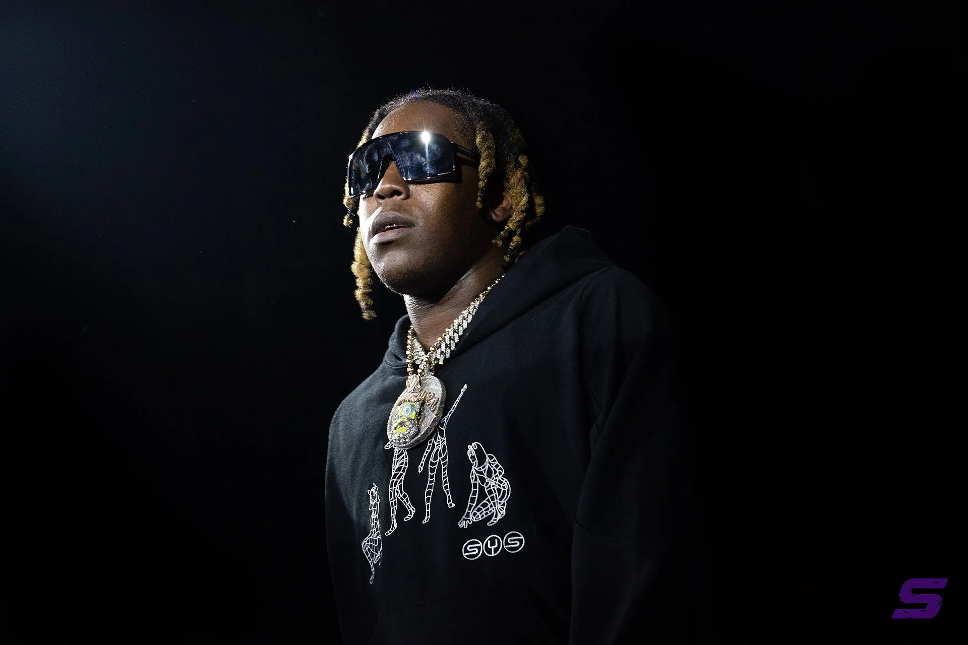 Don Toliver sur scène, lunettes noires et sweat à capuche, sur fond noir