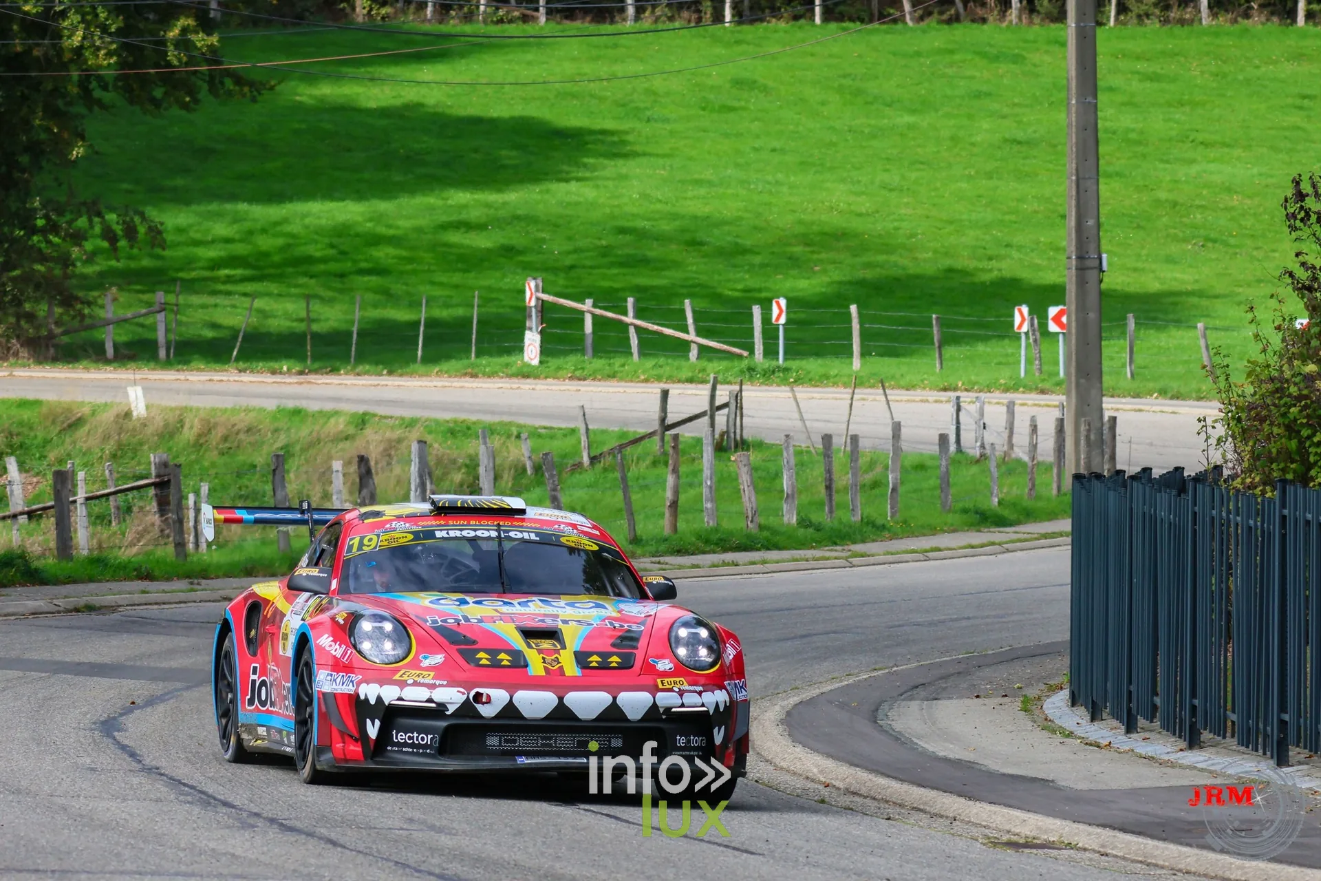 Porsche 911 GT3 de rallye rouge et jaune dans une épingle en village, East Belgian Rally 2026