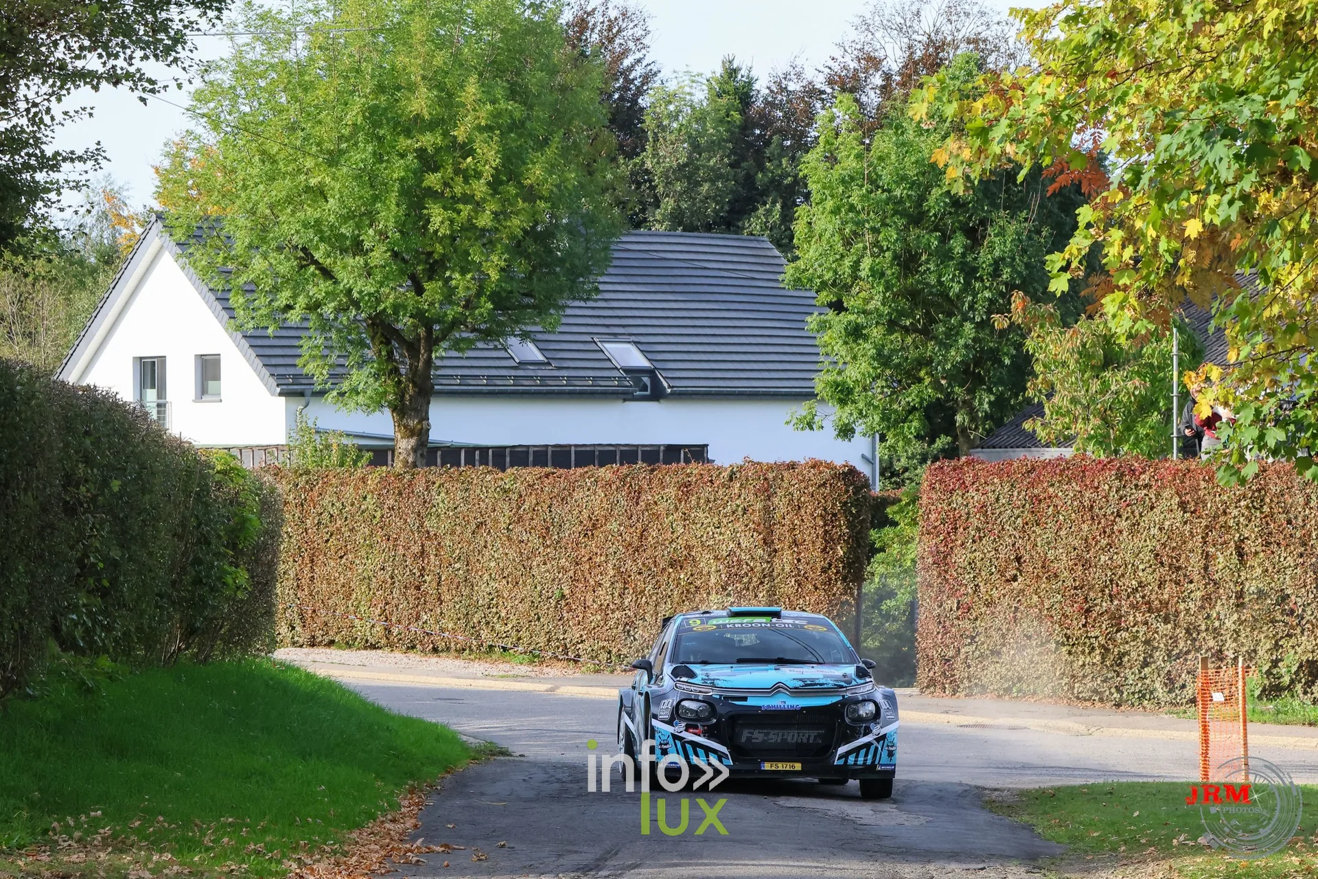 Voiture de rallye bleue au loin devant une maison blanche et une haie, East Belgian Rally 2026
