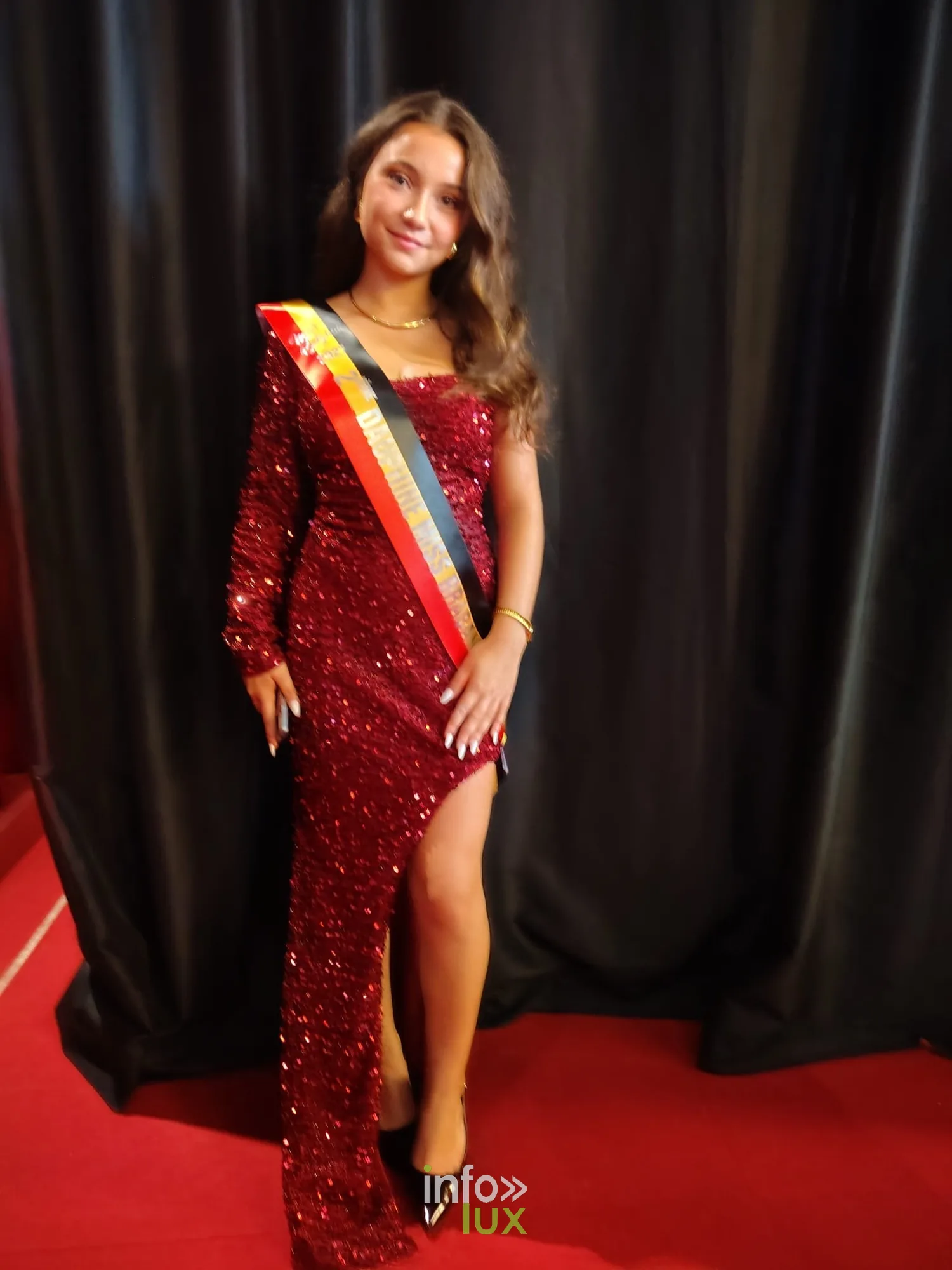 Eléa Colasuonno en robe longue fendue bordeaux devant un rideau noir