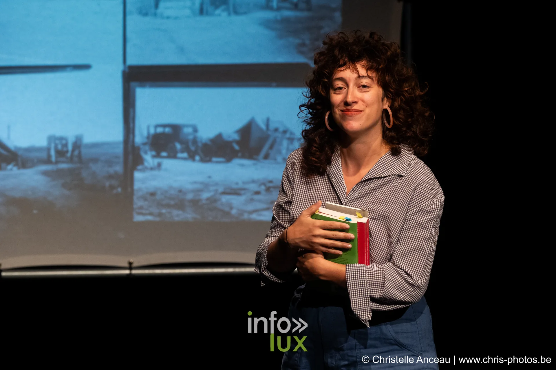 Une comédienne tient des livres devant une image projetée