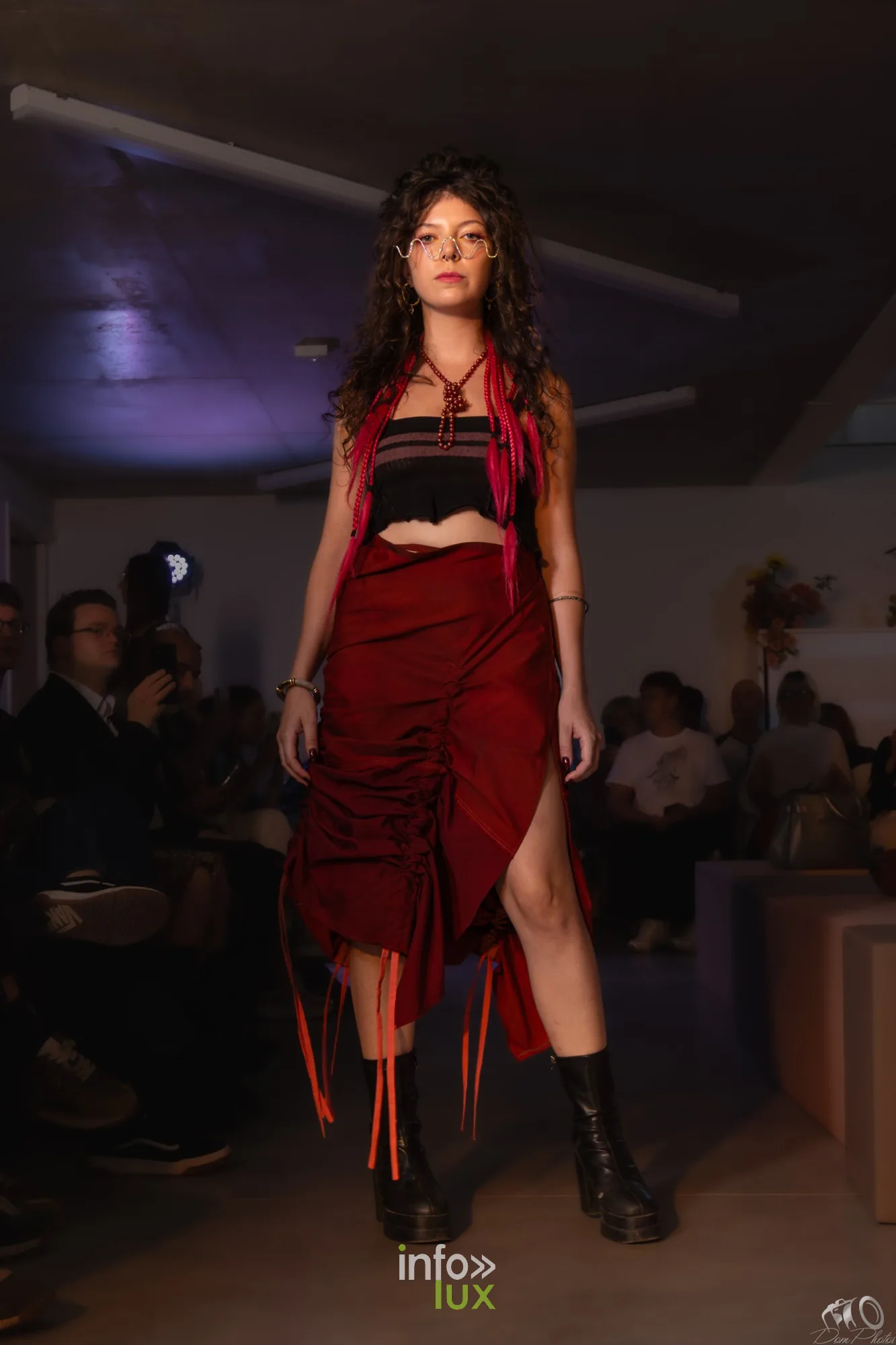 Mannequin aux cheveux bouclés en top noir à franges rouges, jupe rouge asymétrique et bottes noires