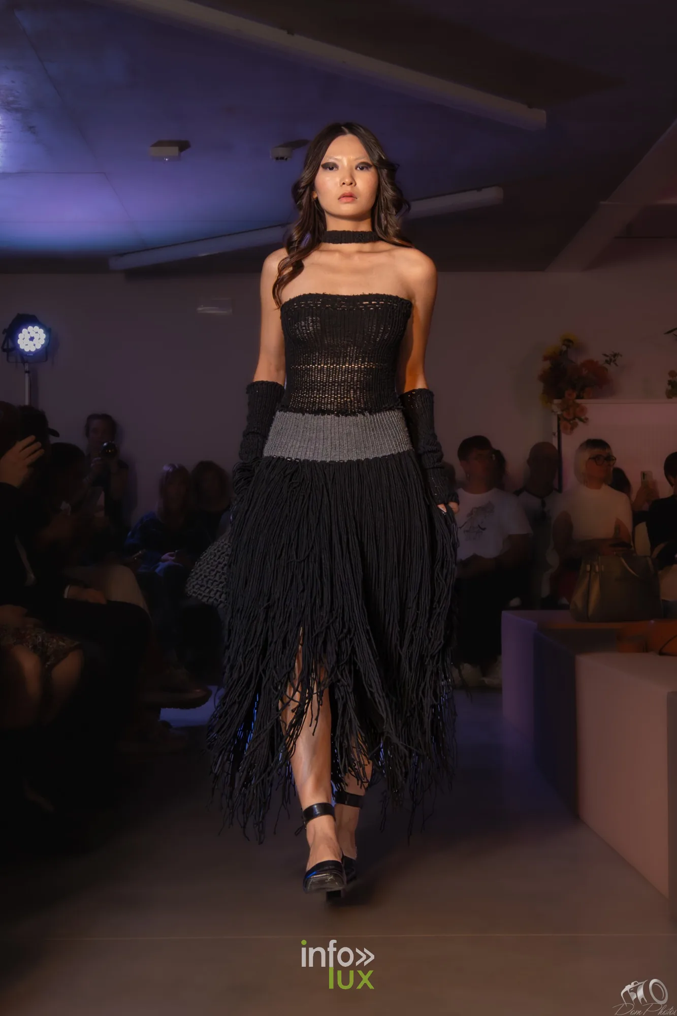Mannequin en robe noire à franges, bustier et longs gants noirs, sur le podium devant le public