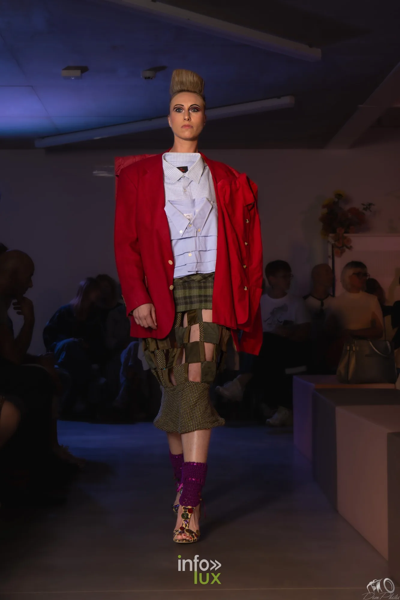 Mannequin en veste rouge oversize, chemise blanche et jupe patchwork kaki, chaussettes bordeaux, sur le podium