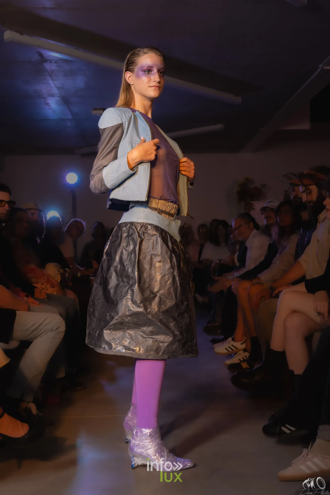 Le même look bleu ciel et jupe noire brillante, de profil, devant le public