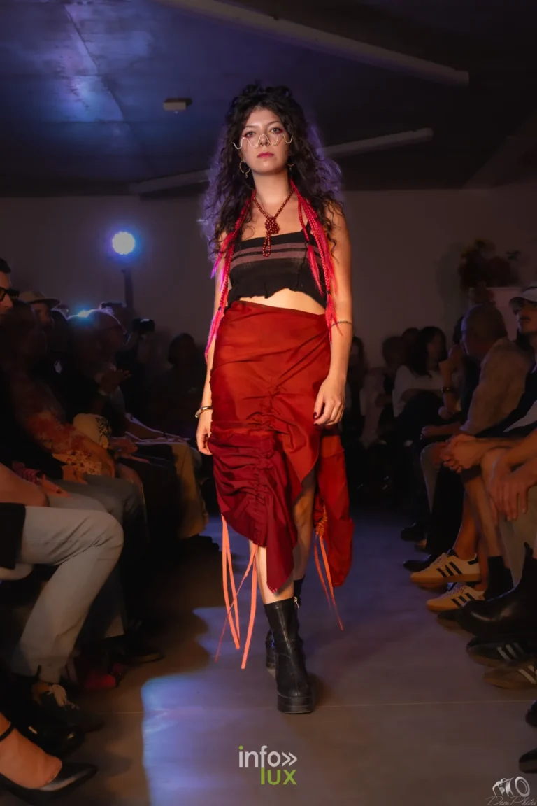 Mannequin aux cheveux bouclés en top noir à franges rouges et jupe rouge asymétrique, en marche sur le podium