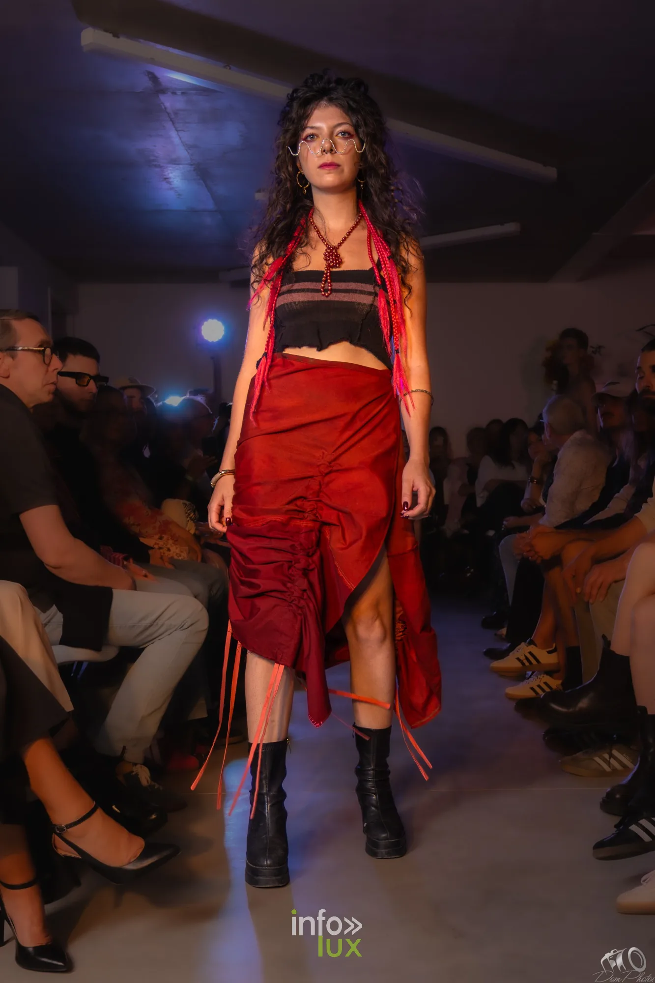 Mannequin en jupe rouge asymétrique et top noir à franges rouges, bottes noires, devant les spectateurs