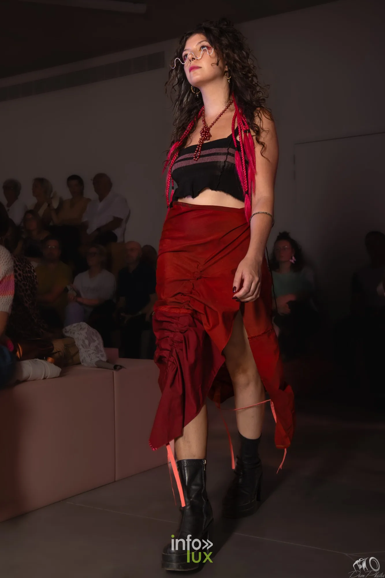 Mannequin en jupe rouge et top noir à franges, regard vers le public, cheveux bouclés