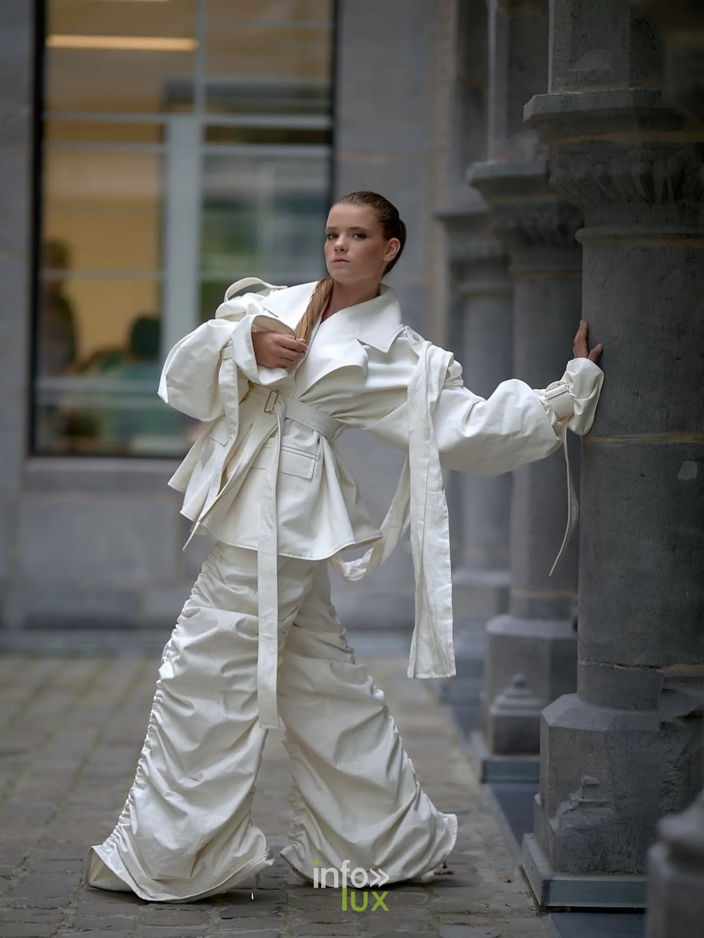 Mannequin en ensemble blanc froncé pose devant les colonnes d’un bâtiment en pierre