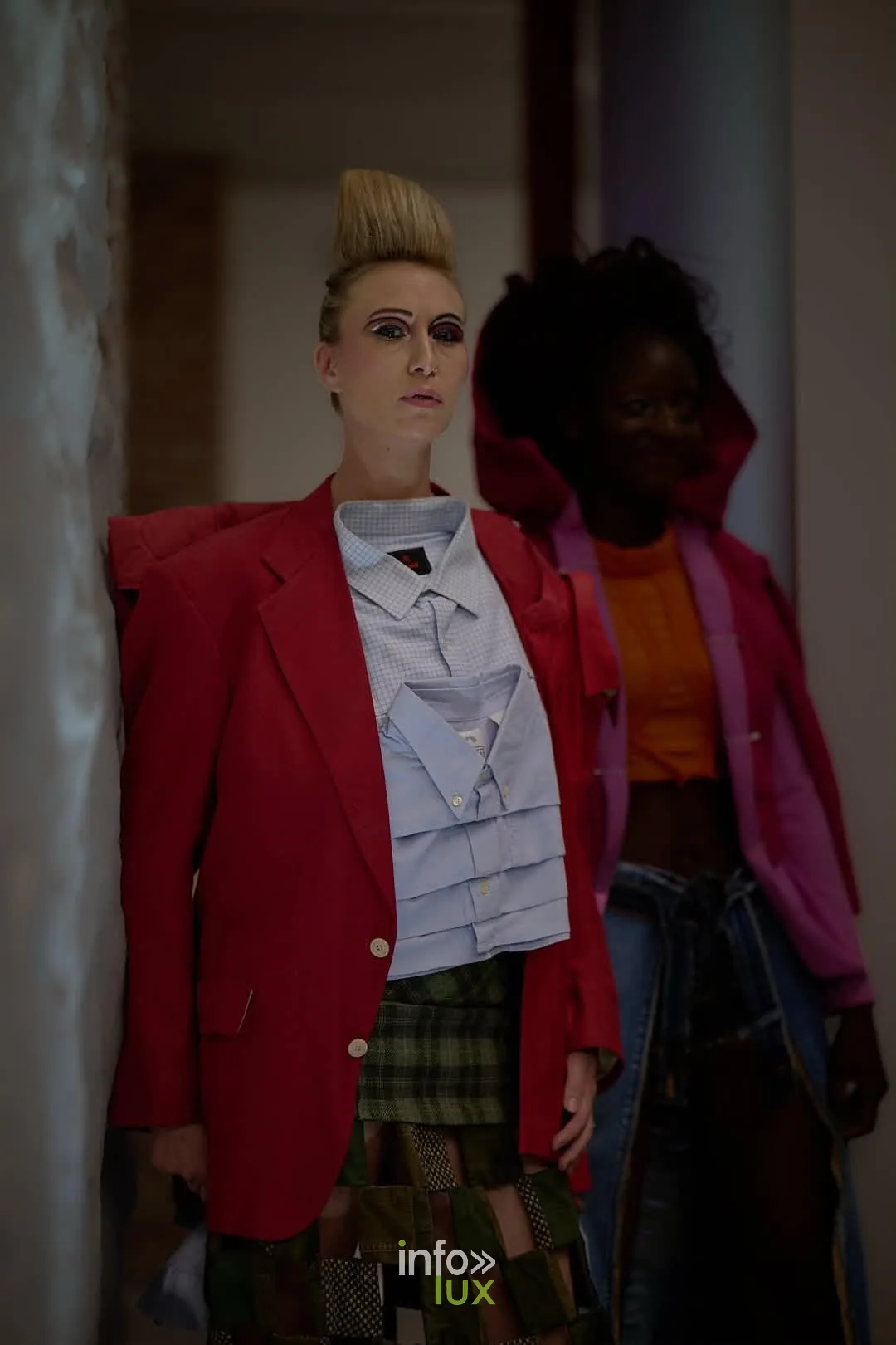 Mannequin à la coiffure crêpée en chemise bleu clair et jupe patchwork, dans la salle du défilé