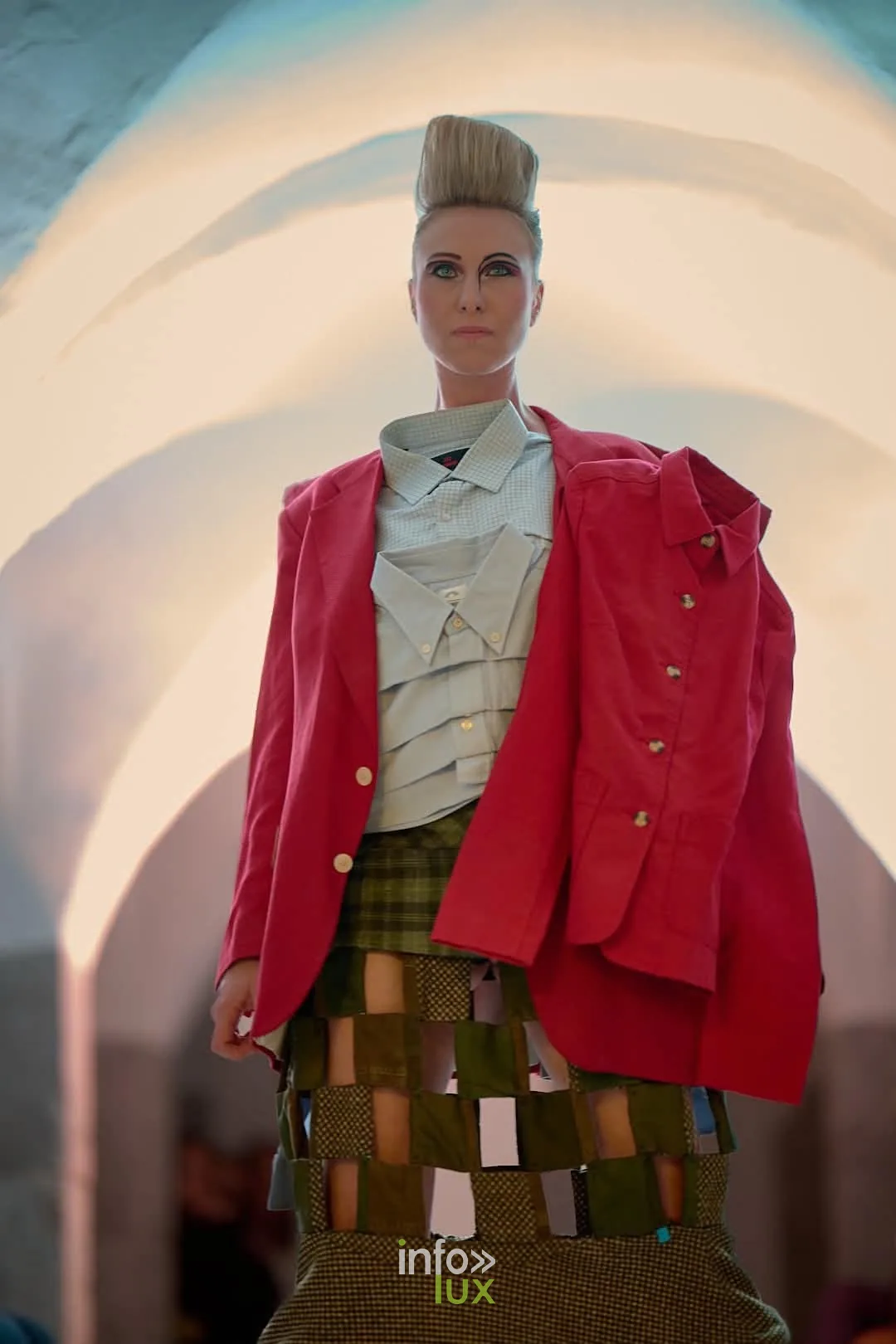 Mannequin en veste rouge et jupe patchwork sous une arche blanche éclairée