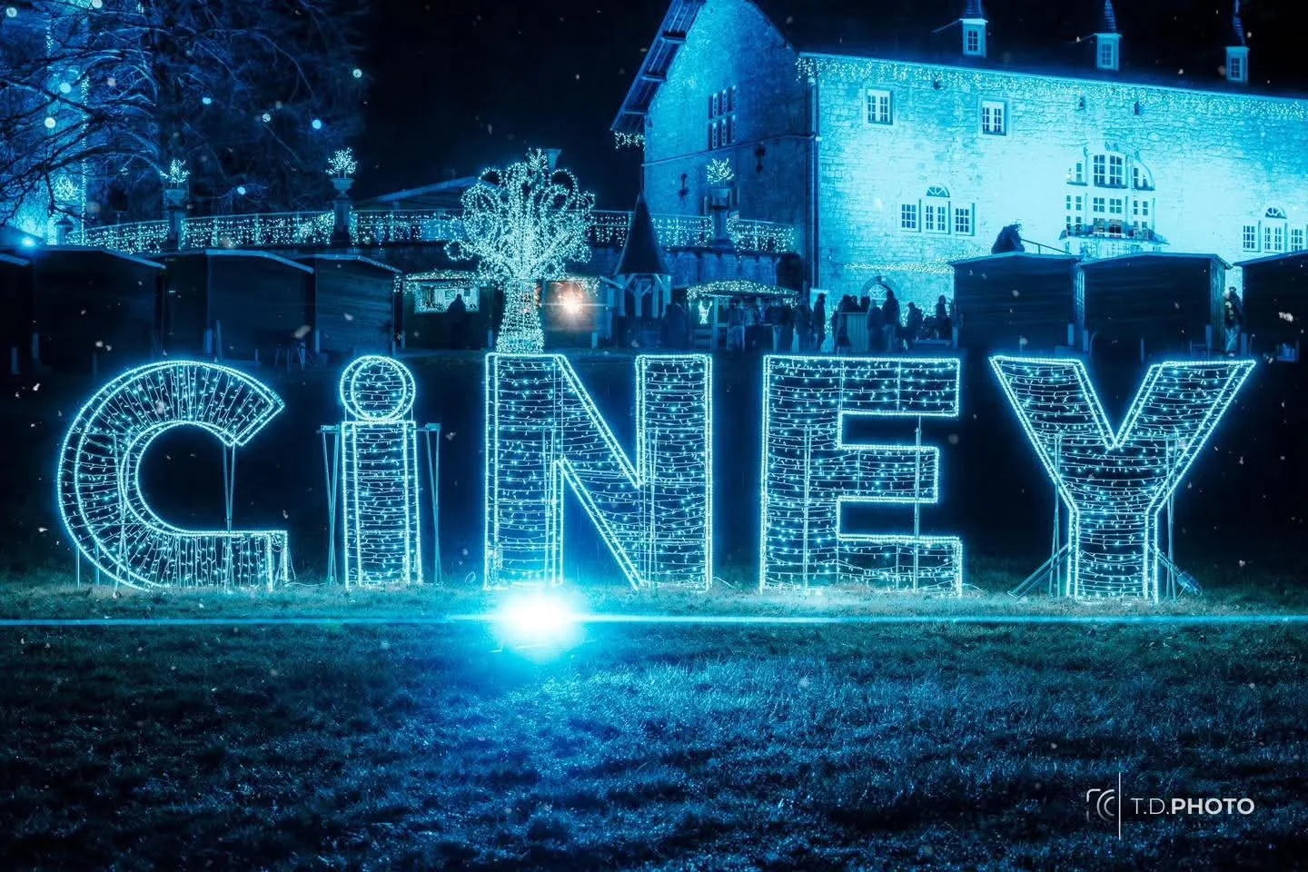 Grandes lettres lumineuses CINEY dans le parc Saint-Roch la nuit, château en fond