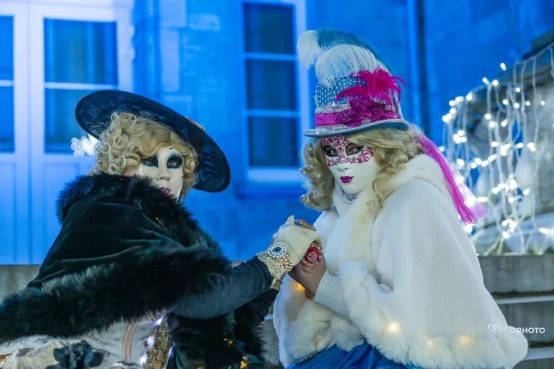 Deux personnages costumés et masqués façon carnaval de Venise devant le château illuminé de Ciney