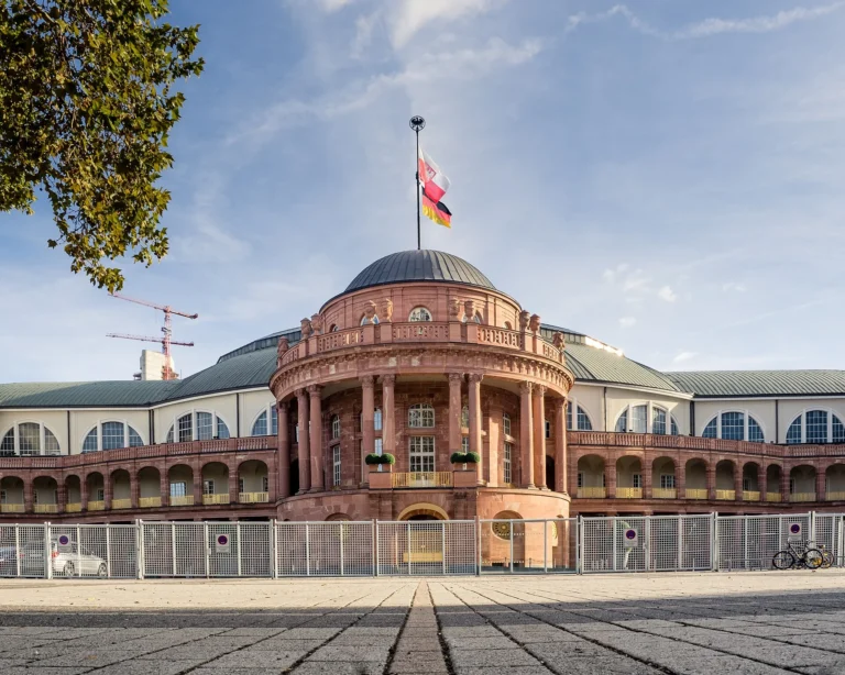 Façade d’entrée en grès rouge de la Festhalle de Francfort, surmontée de drapeaux, sous un ciel bleu