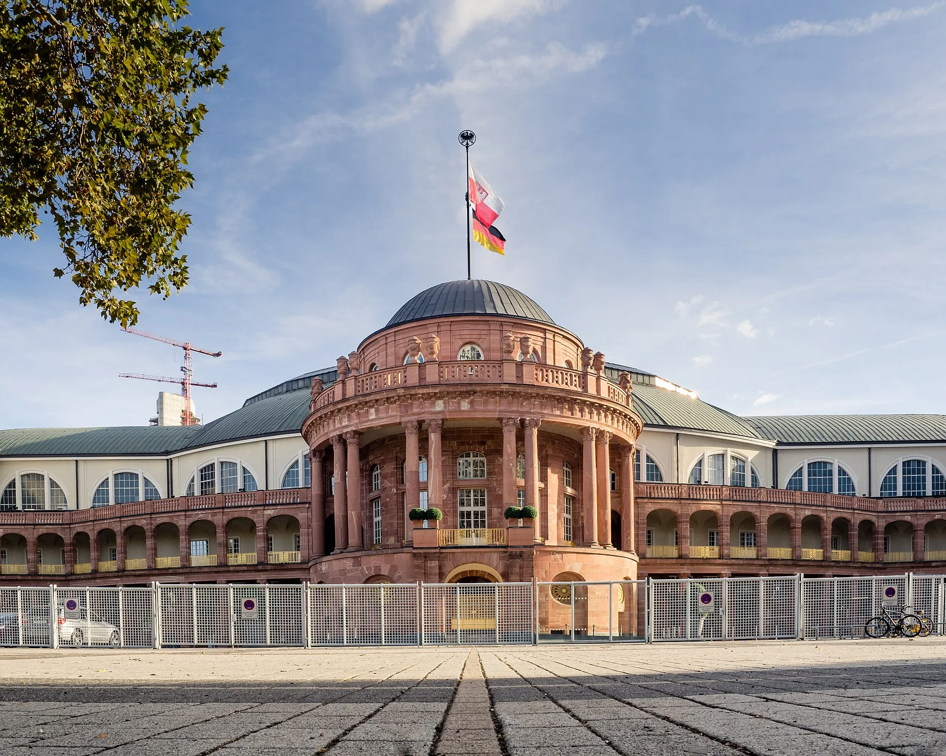 Façade d’entrée en grès rouge de la Festhalle de Francfort, surmontée de drapeaux, sous un ciel bleu