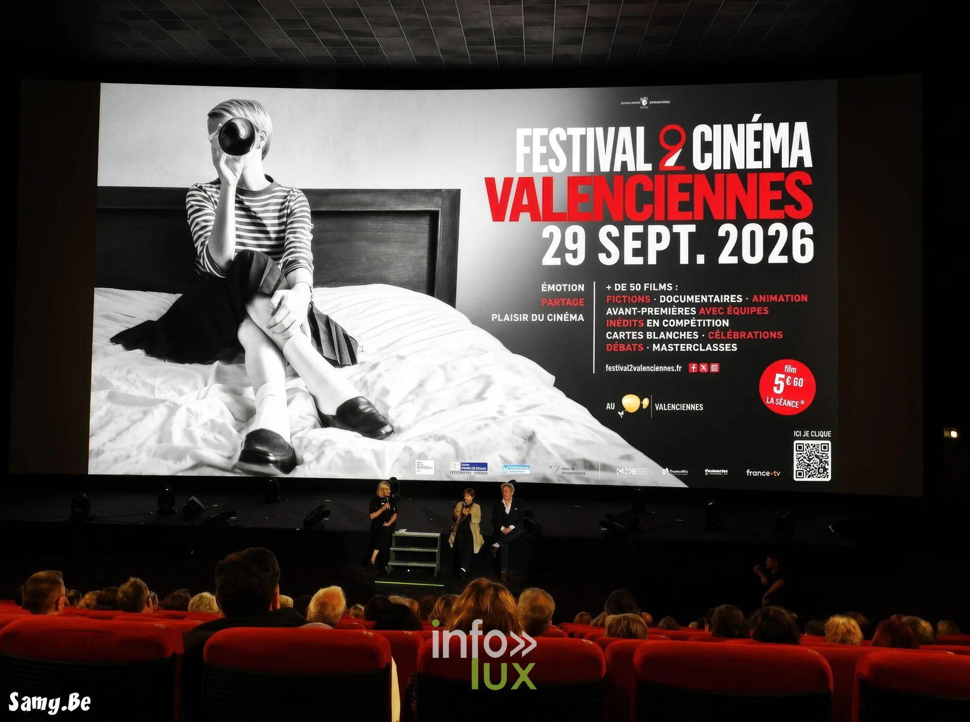 L’affiche du festival sur l’écran, les invités sur scène devant la salle