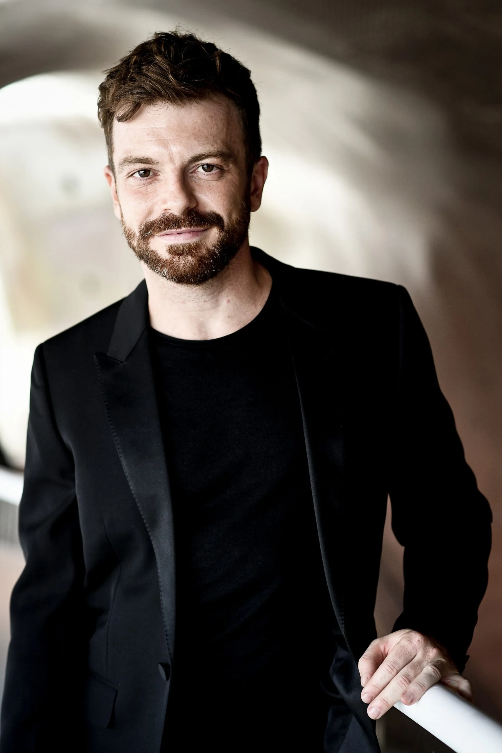Le pianiste David Kadouch, en veste noire, appuyé contre un piano