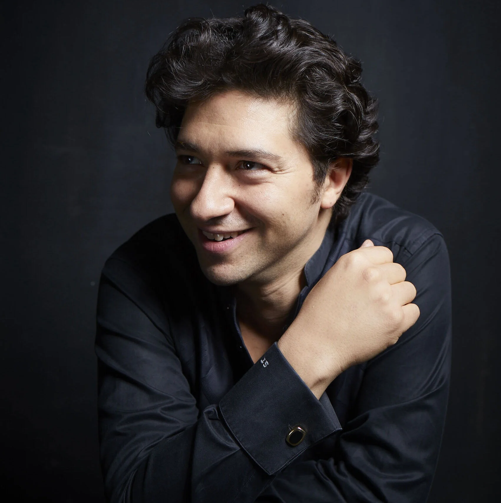 Le pianiste Sergio Tiempo, souriant, les bras croisés sur fond sombre