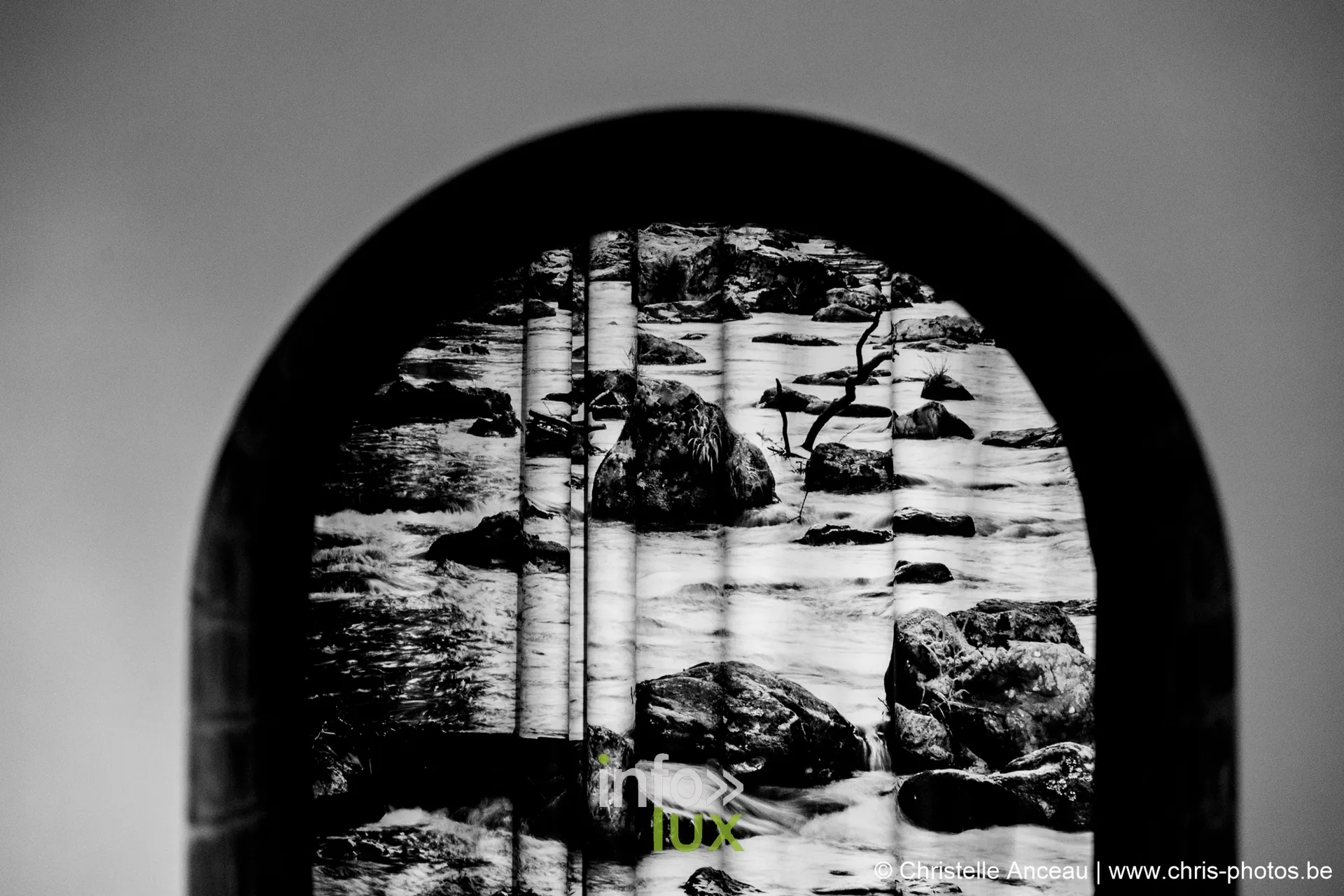 Photographie en noir et blanc d'un cours d'eau, encadrée dans une arche du musée