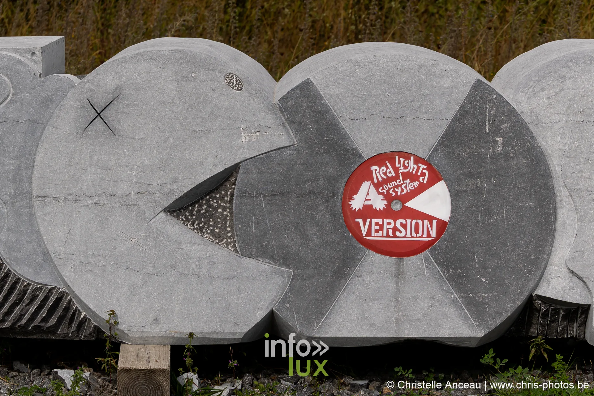 Sculpture en pierre bleue composée de disques, marquée d'un panneau rouge