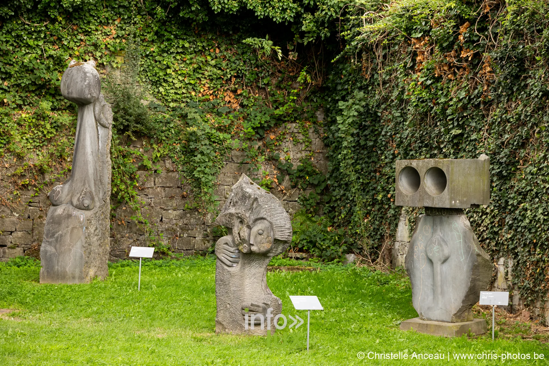 Trois sculptures alignées sur la pelouse devant un mur couvert de lierre