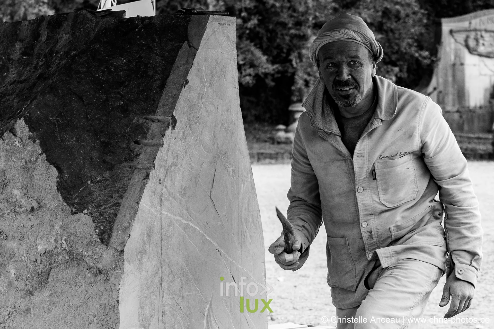 Un sculpteur souriant, assis au pied de l'œuvre qu'il taille