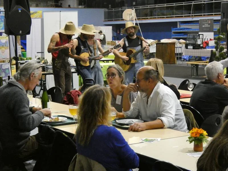 Visiteurs attablés à la restauration bio de la Foire de Gorcy, avec un groupe de musiciens en fond