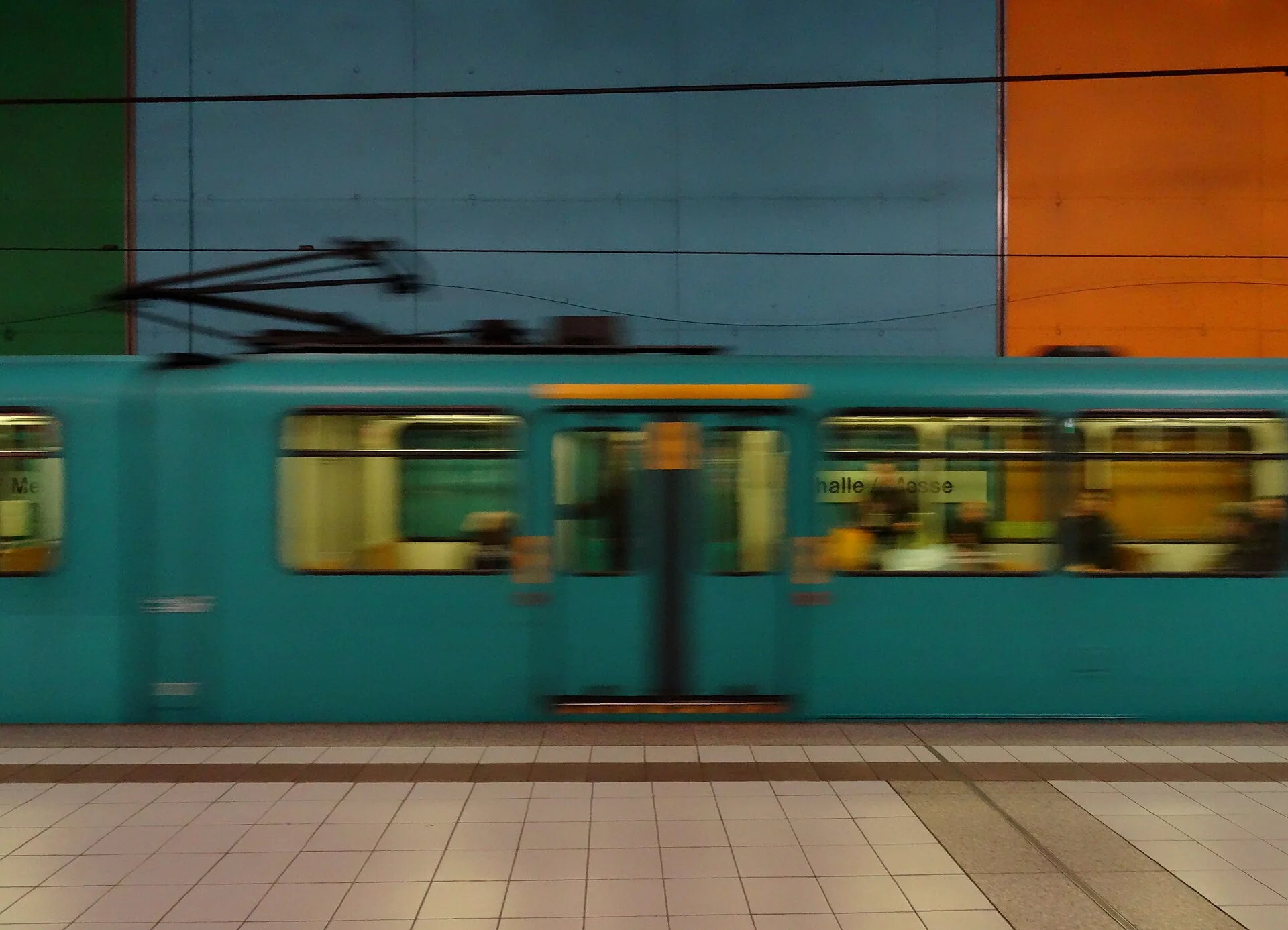 Rame de métro en mouvement dans la station Festhalle/Messe de Francfort, murs bleu, vert et orange