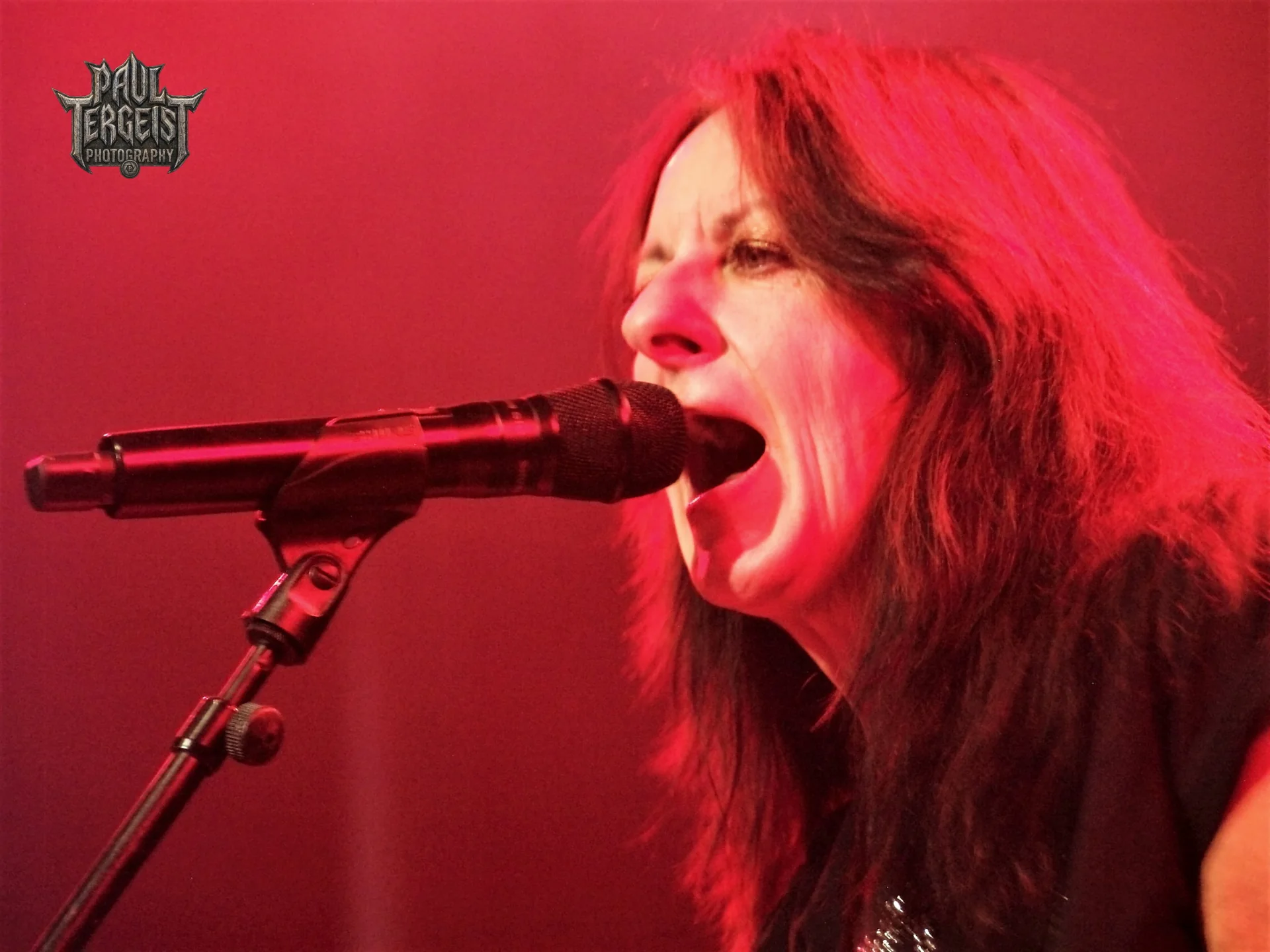 Kim McAuliffe de Girlschool chante au micro sous une lumiere rouge au Golden Age Rock Festival 2023