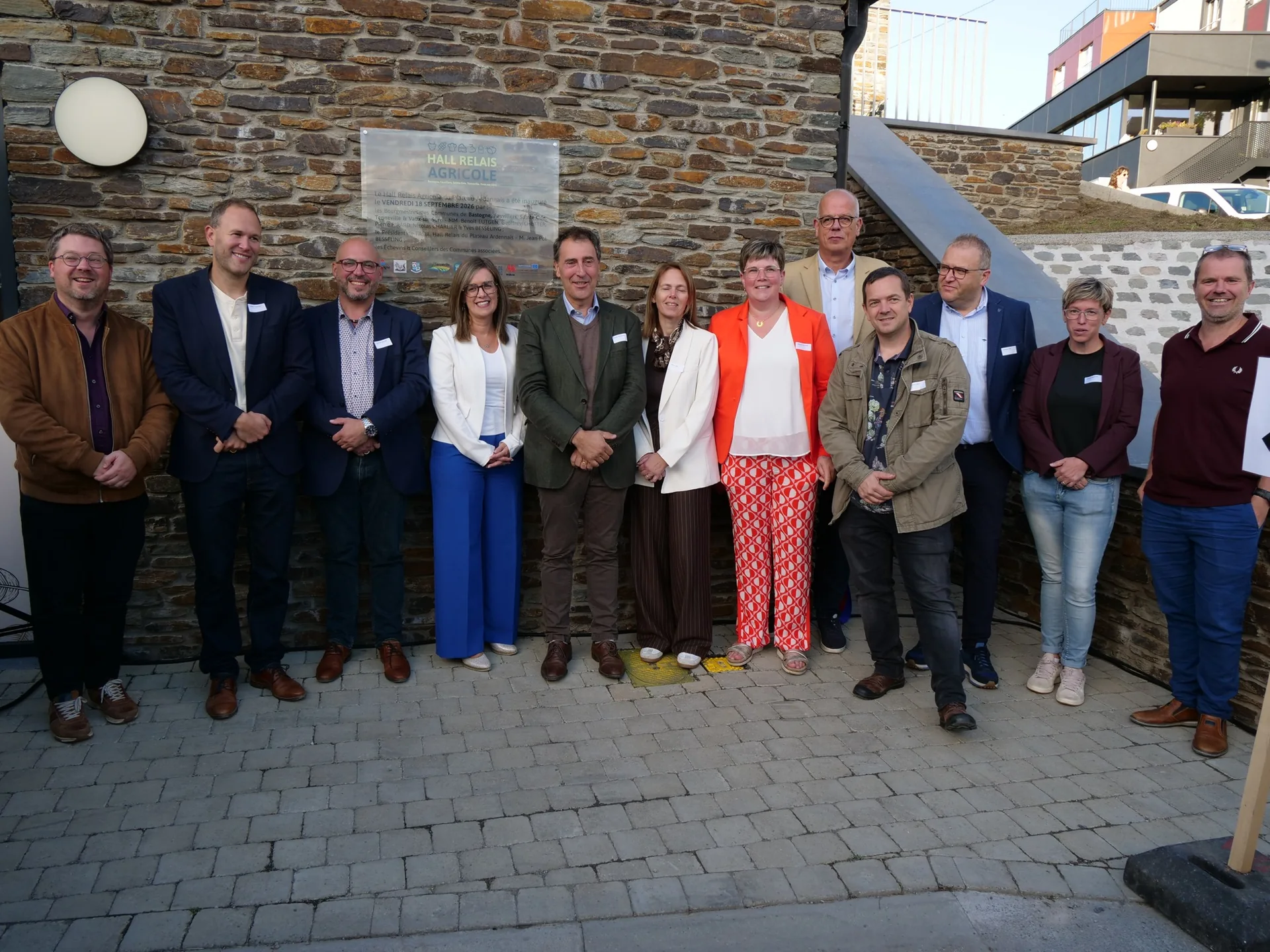 Photo de groupe des élus et partenaires devant le mur en pierre du Hall Relais Agricole du Plateau Ardennais