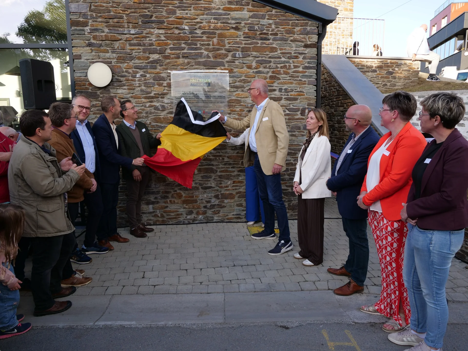 Dévoilement de la plaque du Hall Relais Agricole du Plateau Ardennais, drapeau belge retiré devant les élus et partenaires, à la gare du Sud de Bastogne