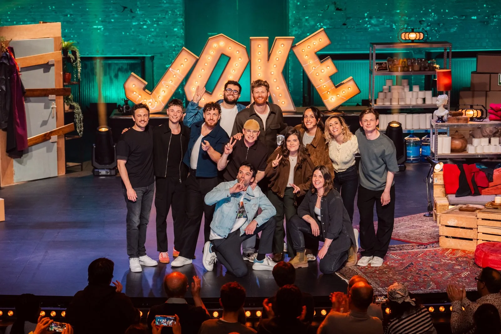 Des humoristes posent sur la scène du Théâtre royal de Namur devant le décor lumineux JOKE, Namur is a Joke 2026