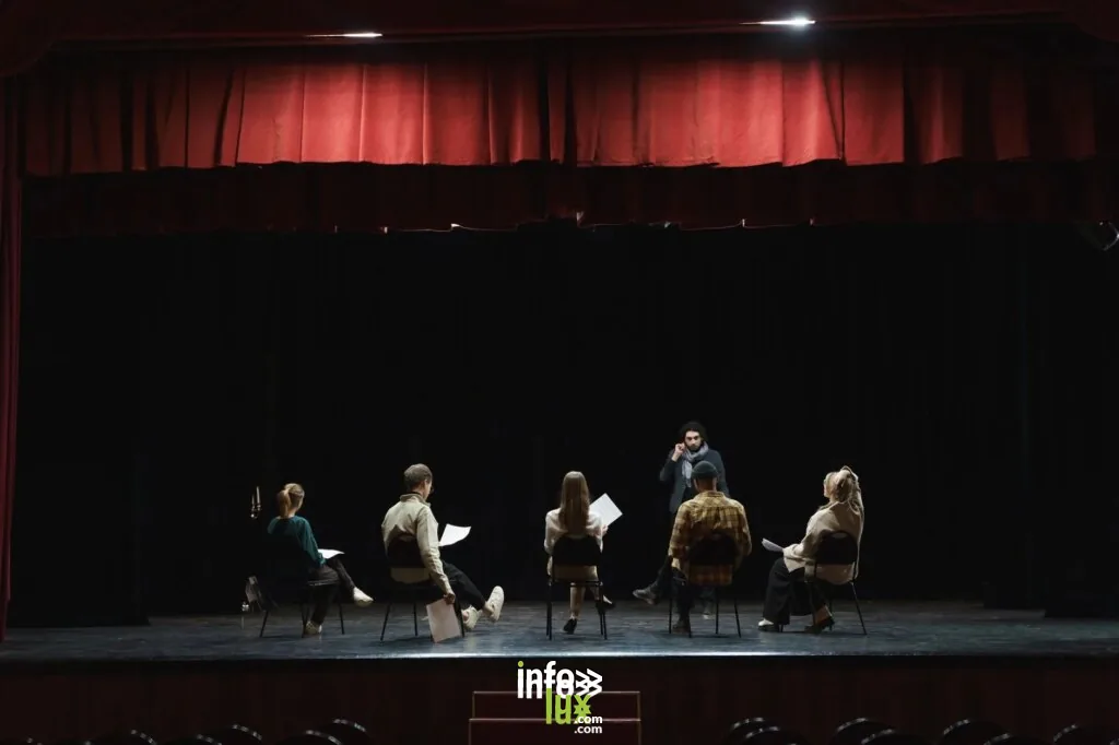 Un groupe d'acteurs répétant sur une scène faiblement éclairée dans un auditorium, préparant une performance de théâtre.