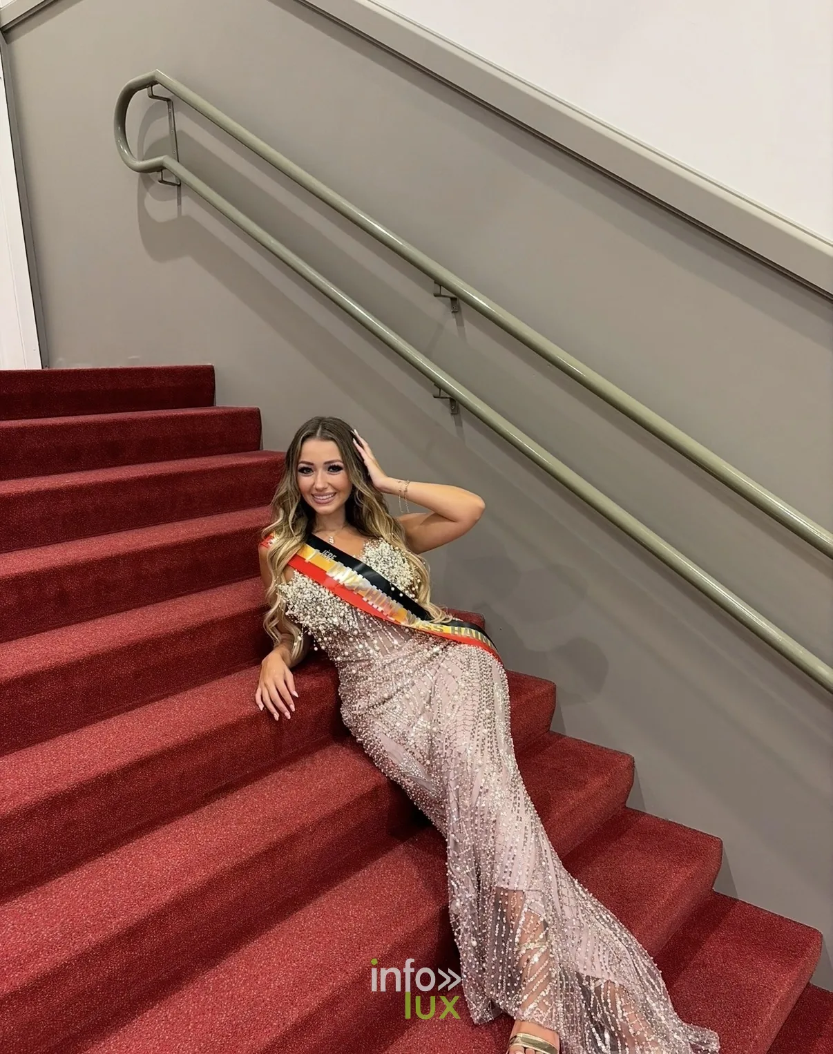 Isaline Dubois allongée sur un escalier au tapis rouge, en robe à paillettes et écharpe