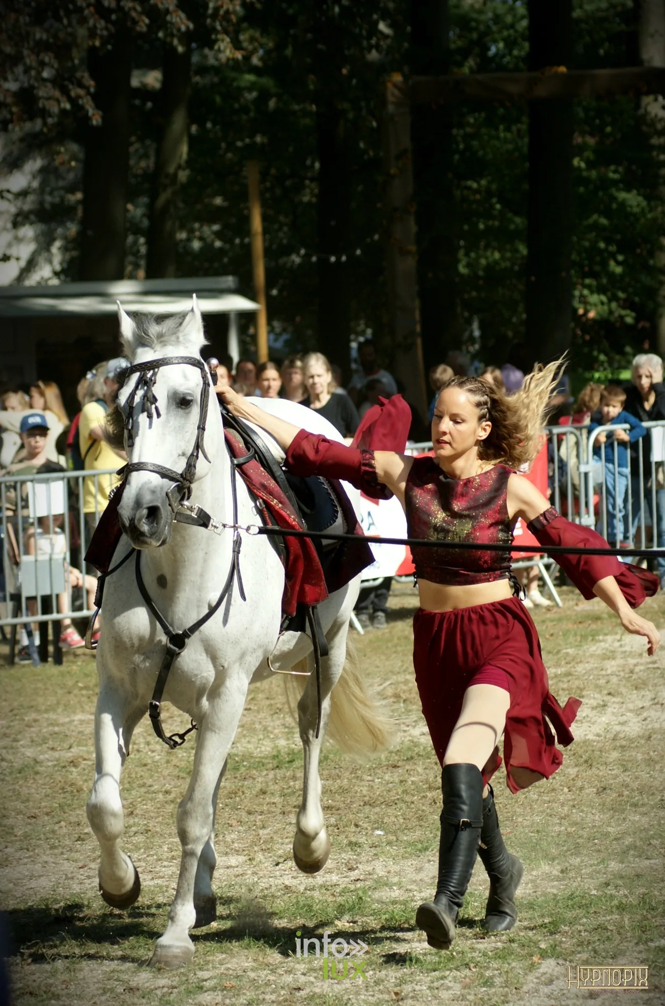 Journées du Cheval 2026 à Braine-l’Alleud, parc du Cheneau : une artiste en costume rouge court aux côtés d’un cheval gris