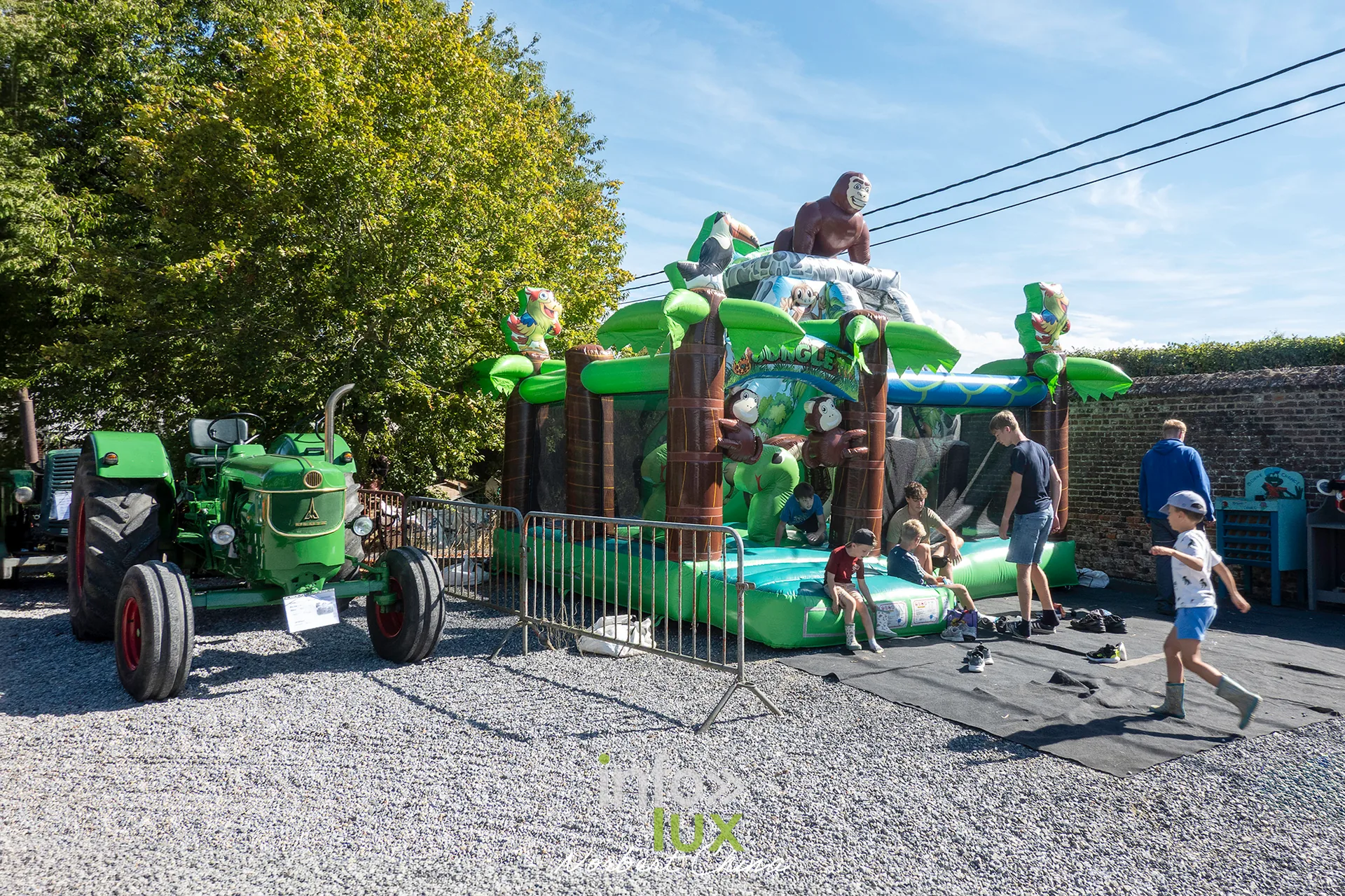 Un château gonflable et un tracteur vert sur le site de la kermesse