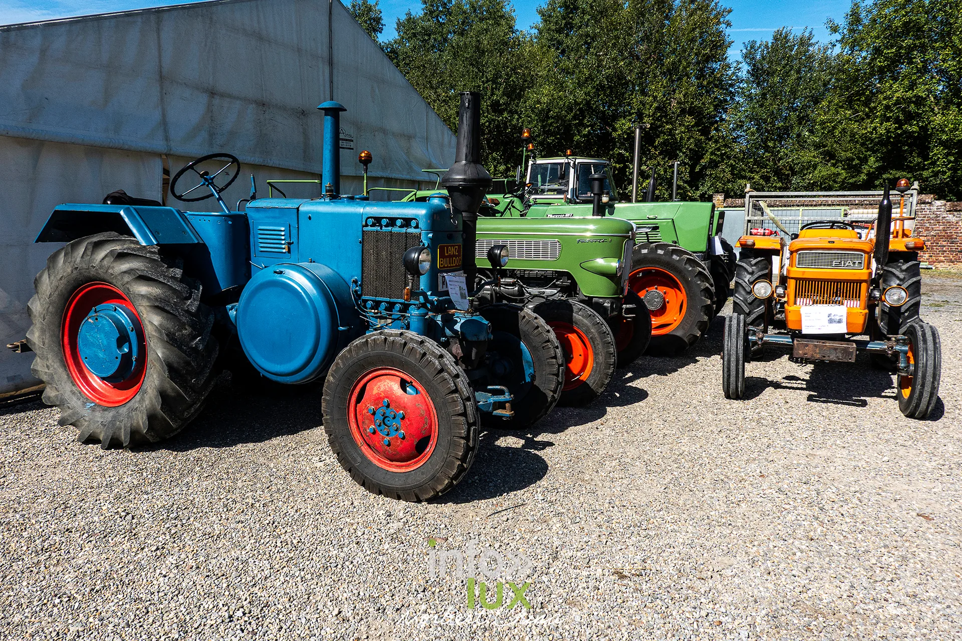 Des tracteurs bleus et verts alignés devant un hangar