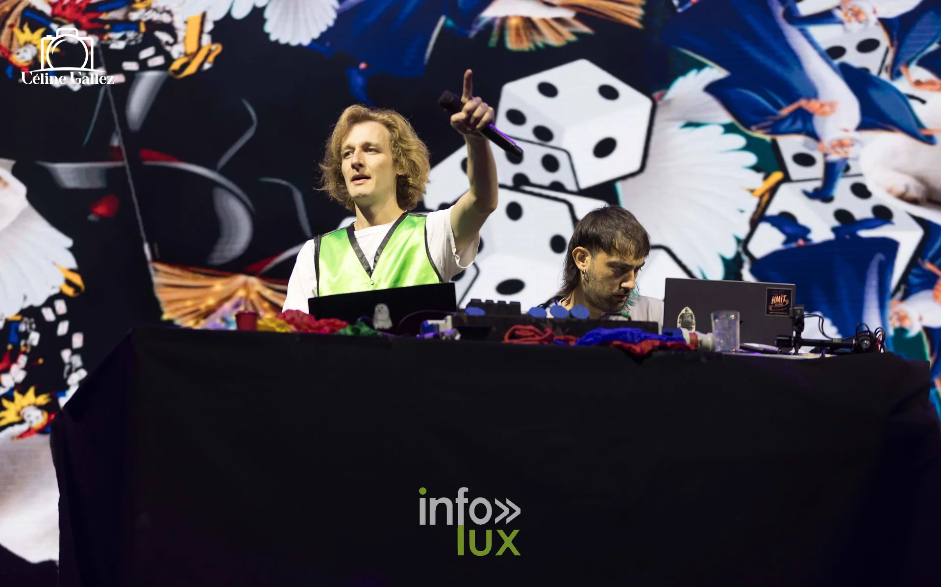 Deux artistes derrière une table de mix, devant un décor coloré