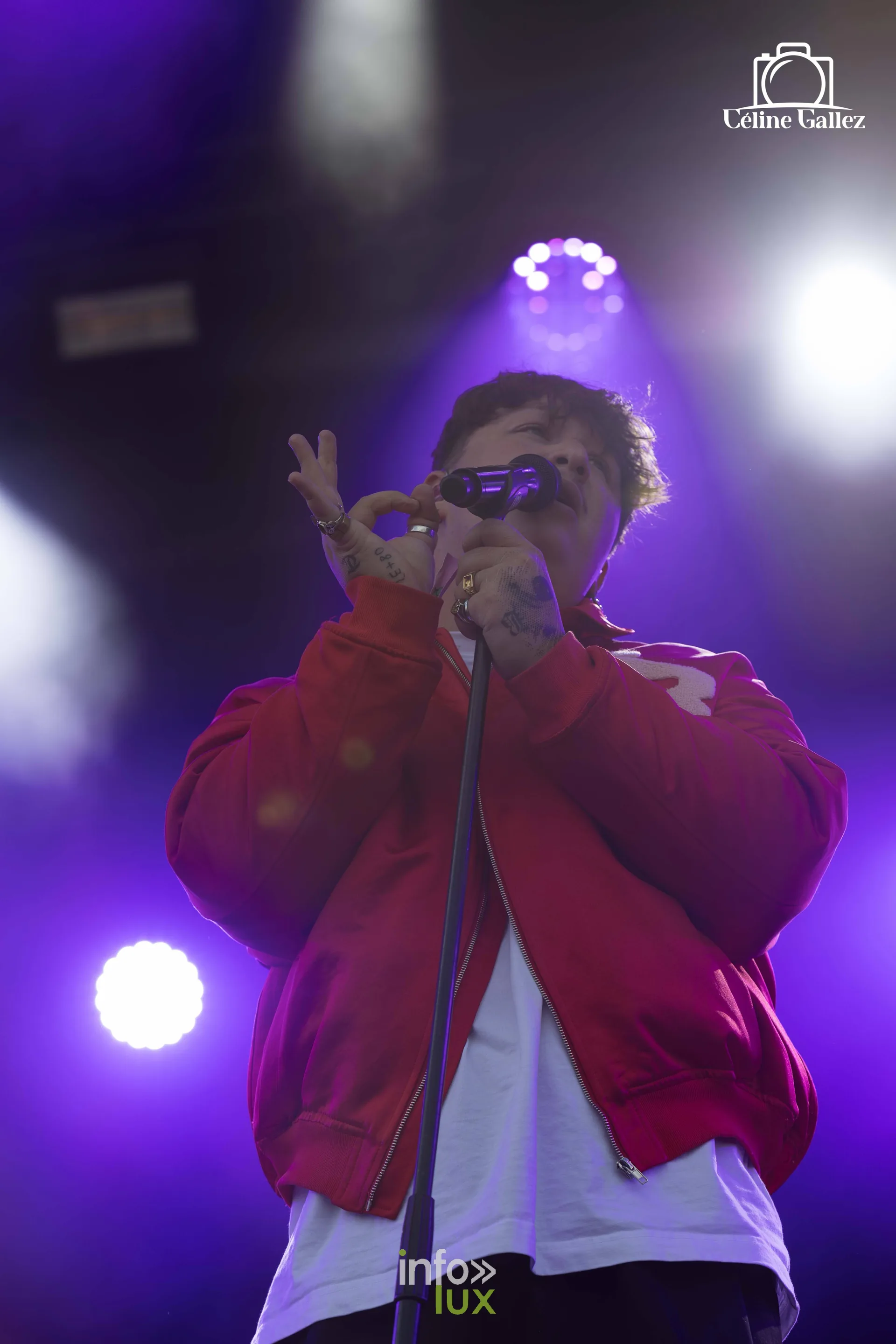 Un artiste en veste rouge et lunettes chante sous une lumière violette
