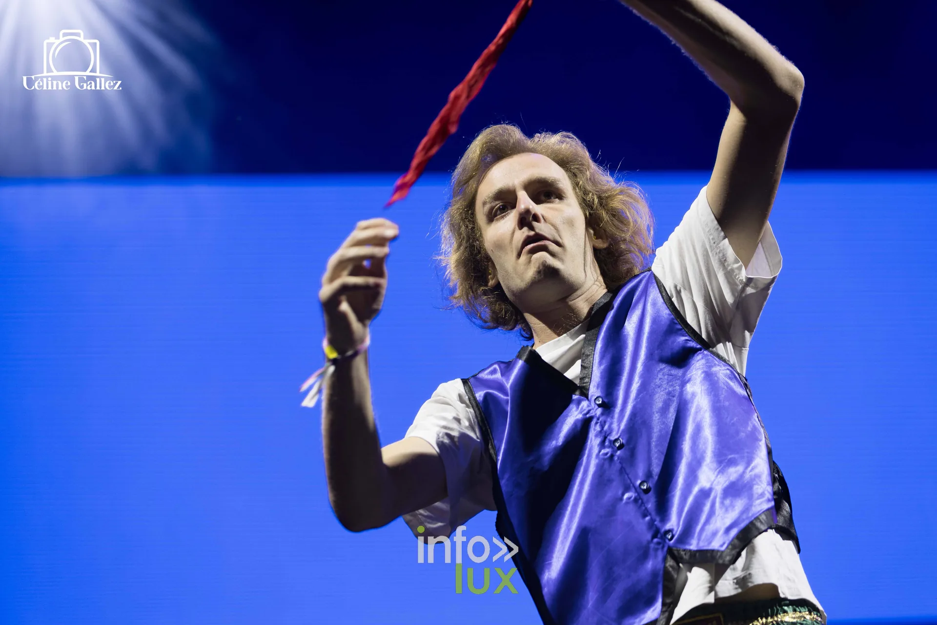 Un artiste bras levé, gilet bleu, devant un fond bleu