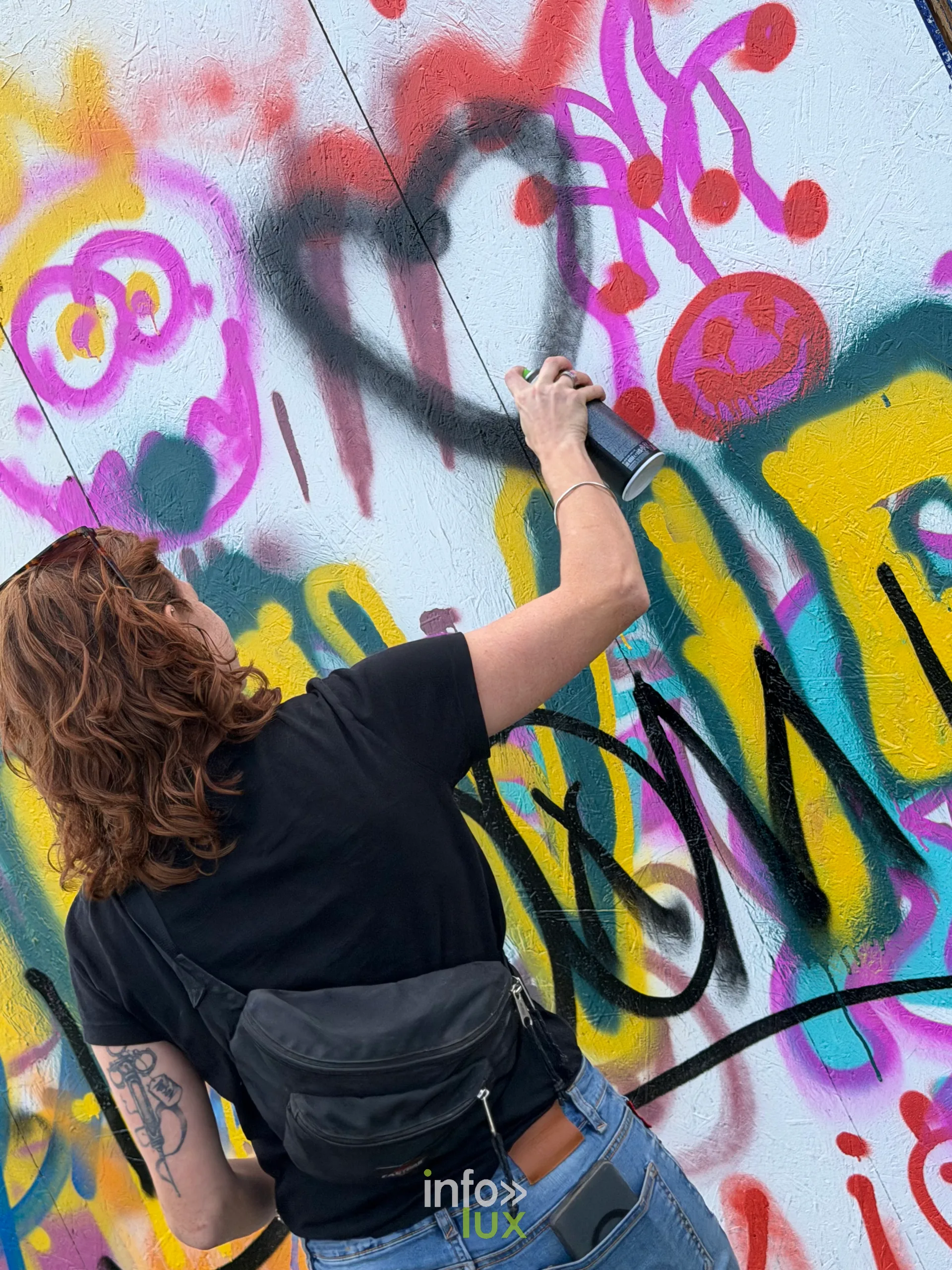 Une festivalière peint sur un mur de graffitis participatif