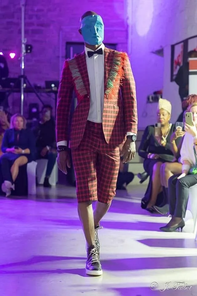 Mannequin masqué en costume à carreaux rouge sur le podium de la Liège Fashion Week