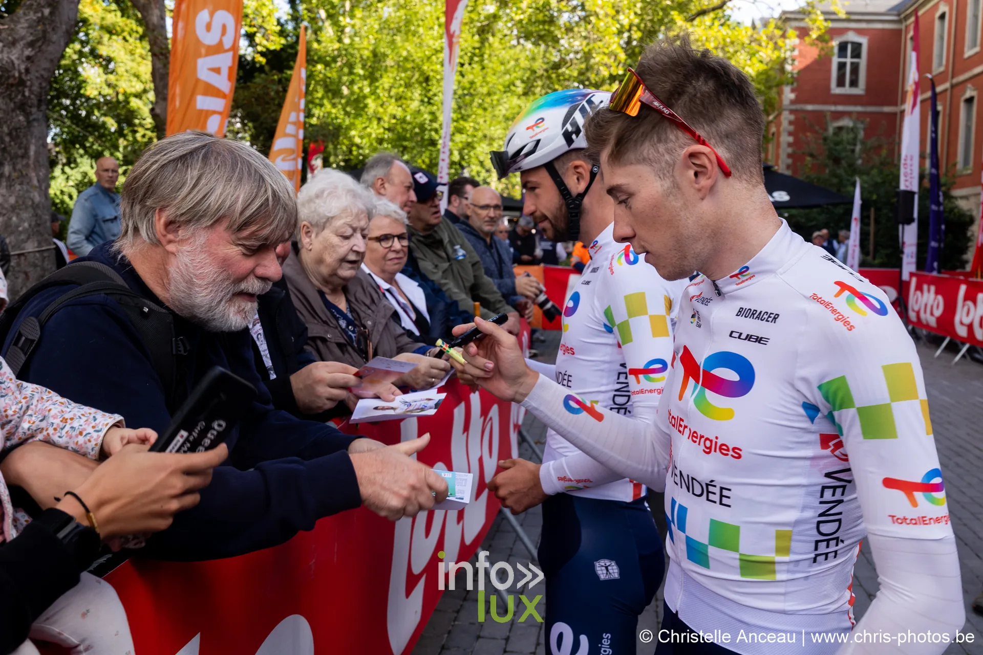 Coureur en maillot blanc TotalEnergies dedicace une carte a un spectateur