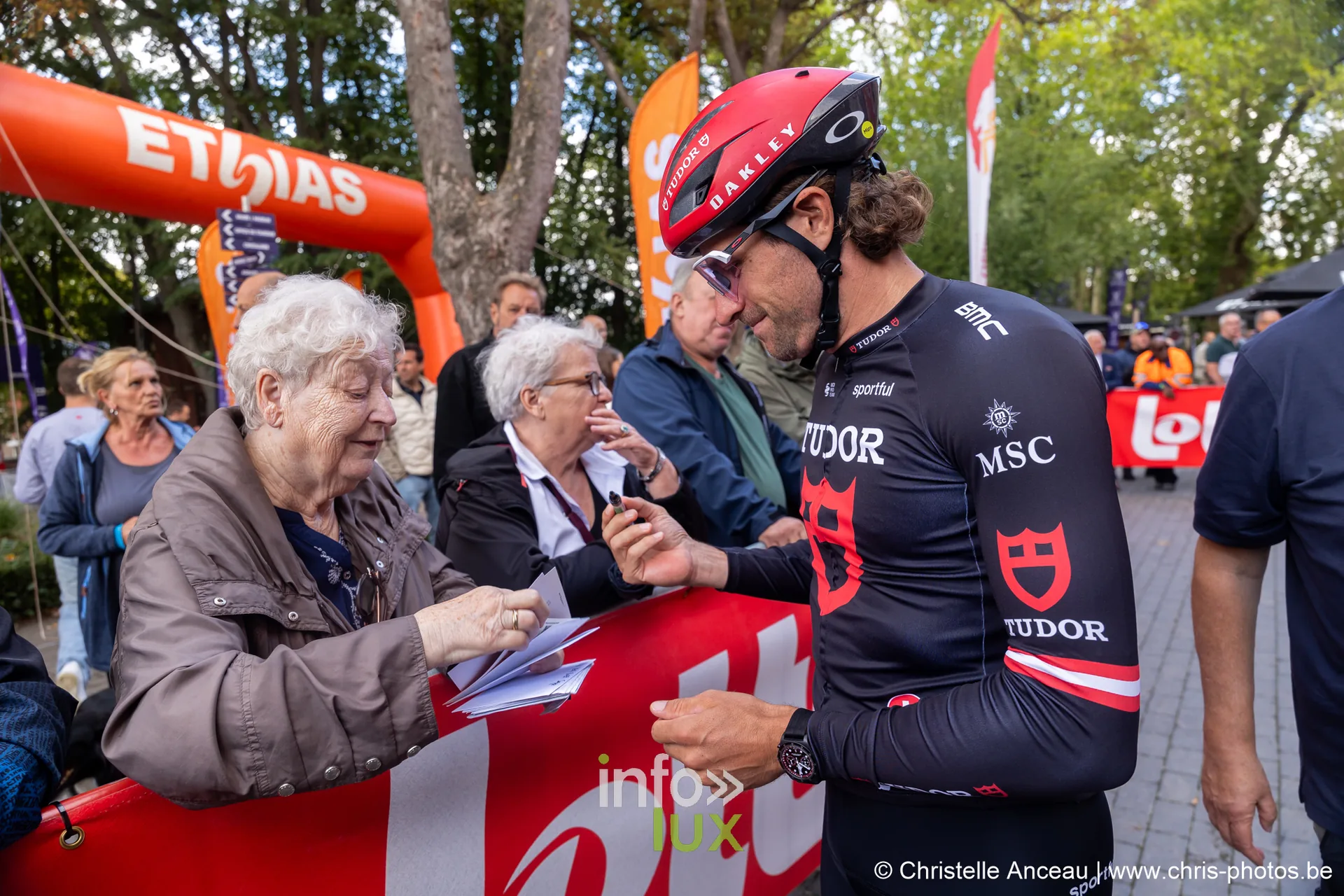 Coureur de l equipe Tudor en noir signant un autographe pour une spectatrice