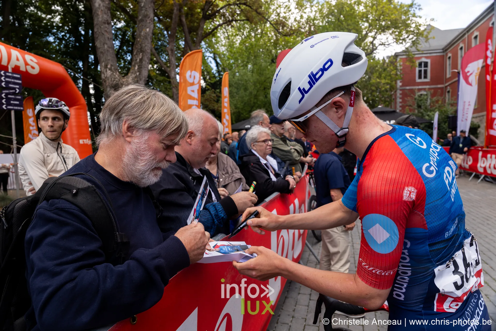 Coureur en maillot bleu et rouge signe pour des spectateurs derriere les barrieres Lotto