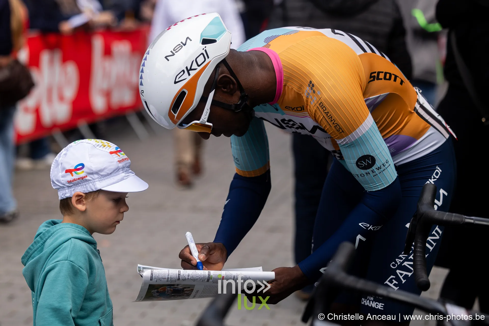Un jeune garcon fait signer sa carte par un coureur en maillot jaune et bleu