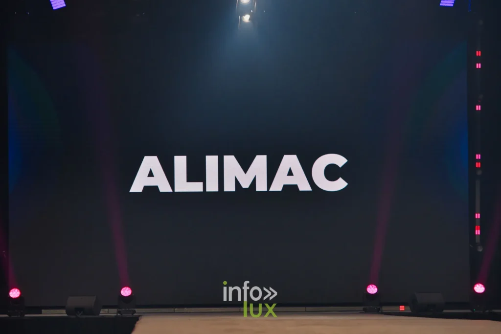 Le nom ALIMAC affiché sur l’écran de scène avant le passage — Alimac, « Mystic Blossom », Lux Fashion Week 2026, Arlon