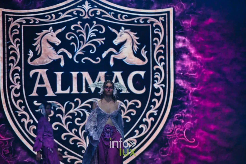 Premières silhouettes lilas devant le blason ALIMAC aux deux licornes projeté à l’écran — Alimac, « Mystic Blossom », Lux Fashion Week 2026, Arlon